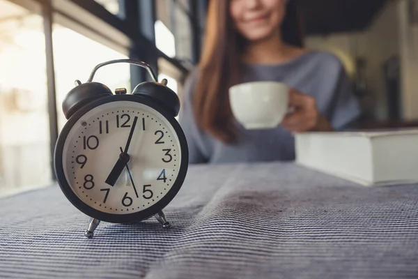 テーブルの上に黒い目覚まし時計と朝の美しいアジアの女性のコーヒーを飲む — ストック写真
