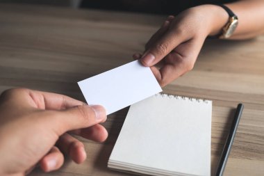 İşadamı, iş kadınına boş bir kartvizit veriyor. Elinde tahta bir defter var. 