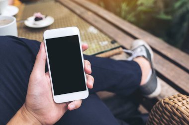 Kafede boş siyah ekranlı beyaz cep telefonu tutan bir adamın görüntüsü.