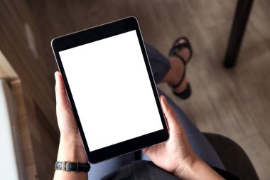 Ofiste boş beyaz masaüstü ekranlı siyah tablet bilgisayarı tutan ve bacak bacak üstüne atmış bir kadının en üst görünüm görüntüsü