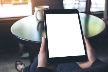 Siyah tabletli, beyaz ekranlı ve kafedeki kahve fincanının olduğu ellerin görüntüsü. 