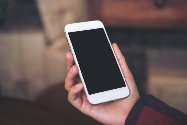 Kafedeki boş siyah ekranlı beyaz cep telefonlu el görüntüsü.