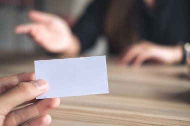 Arka planda iş kadını olan boş bir kartvizit tutan bir işadamı.