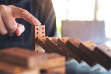 Tahta domino oyununun masaya düşmesini engellemeye çalışan bir elin yakın plan görüntüsü.