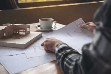 Mimari bir model üzerinde çalışan bir mimar. Masaya kağıt ve kahve fincanı çiziyor.