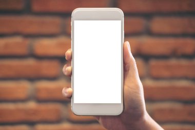 El ele tutuşmanın ve beyaz cep telefonunu tuğla duvar zeminli boş masaüstü ekranıyla kaldırmanın görüntüsü