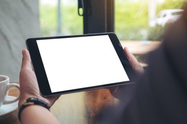Siyah tabletli, beyaz ekran ve kafedeki ahşap masada kahve fincanı tutan bir kadının ellerini taklit et.