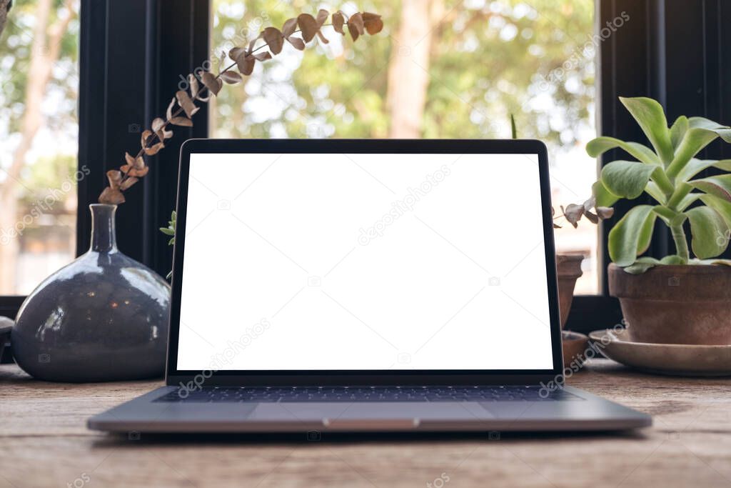 Mockup image of laptop with blank white desktop screen and coffee cup on vintage wooden table in cafe