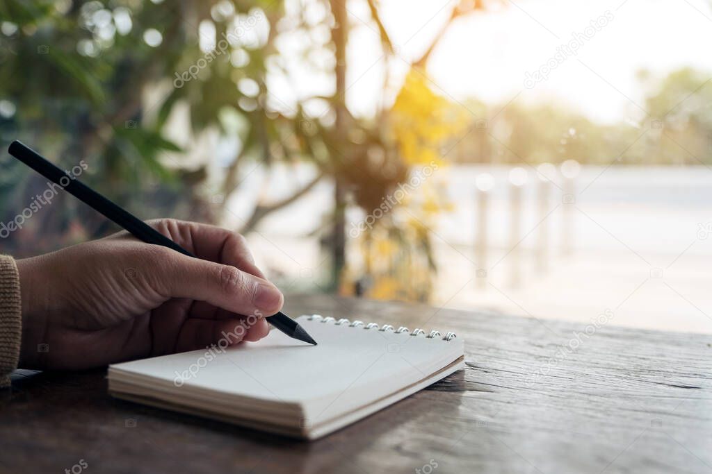 Closeup image of hand writing down on a blank notebook on wooden table 