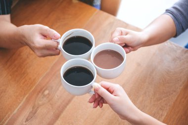 Kahve fincanlarını kafedeki ahşap masaya tokuşturan üç kişinin en iyi görüntüsü.