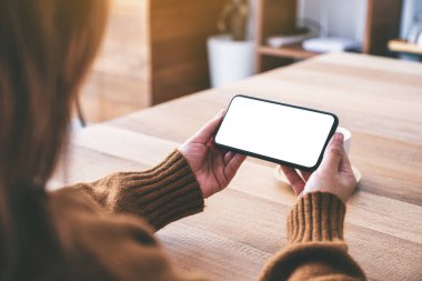 Masasında kahve fincanı olan ve elinde boş masaüstü ekranı olan siyah bir cep telefonu tutan bir kadının görüntüsü.