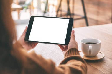 Siyah tabletli, beyaz ekranlı ve ahşap masada kahve fincanı olan ellerin görüntüsü. 