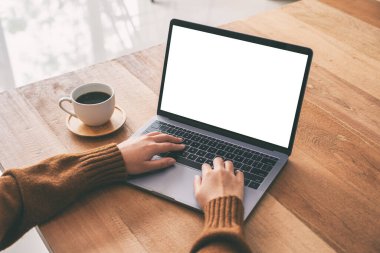 Laptop bilgisayar klavyesinde boş beyaz masaüstü ekran ve ahşap masada kahve fincanı kullanan ve daktilo kullanan bir kadının görüntüsü. 