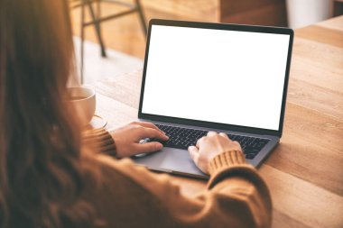 Laptop bilgisayar klavyesinde boş beyaz masaüstü ekran ve ahşap masada kahve fincanı kullanan ve daktilo kullanan bir kadının görüntüsü. 