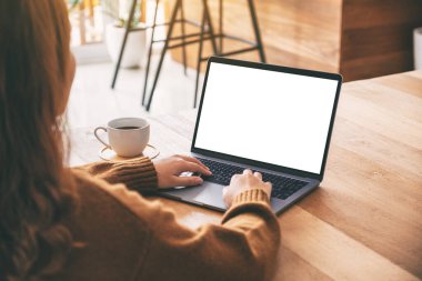 Laptop bilgisayar klavyesinde boş beyaz masaüstü ekran ve ahşap masada kahve fincanı kullanan ve daktilo kullanan bir kadının görüntüsü. 