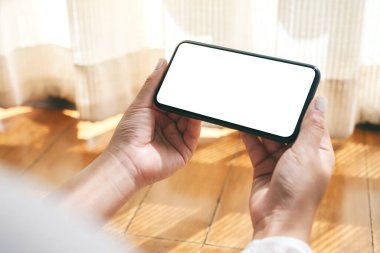 Boş masaüstü ekranı olan siyah cep telefonunu yatay olarak tutan ve kullanan elleri görüntüle 