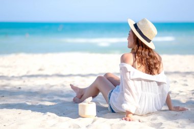 Güzel Asyalı bir kadının portre resmi sahilde oturup hindistan cevizi suyu içmekten zevk alır.