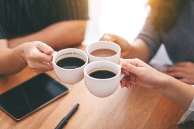 Kahve fincanlarını kafedeki ahşap masaya tokuşturan üç kişinin en iyi görüntüsü.