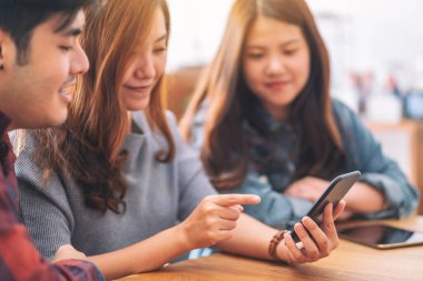 Toplantıda aynı cep telefonunu kullanan ve ona bakan üç Asyalı genç insan.