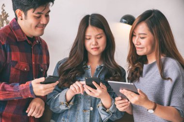 Cep telefonu ve tablet bilgisayarı kullanan ve ona bakan üç Asyalı genç.