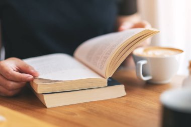 Yakından bakınca, elinde kitap tutan ve kitap okuyan bir kadının resmi. Üzerinde kahve fincanı olan ahşap bir masa.