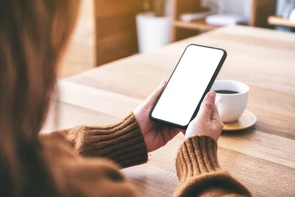 Masasında kahve fincanı olan ve elinde boş masaüstü ekranı olan siyah bir cep telefonu tutan bir kadının görüntüsü.