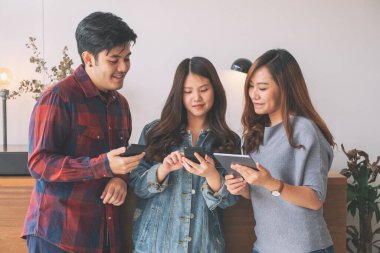 Cep telefonu ve tablet bilgisayarı kullanan ve ona bakan üç Asyalı genç.