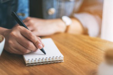 Tahta masaya boş bir deftere yazı yazan bir kadının yakın plan resmi. 