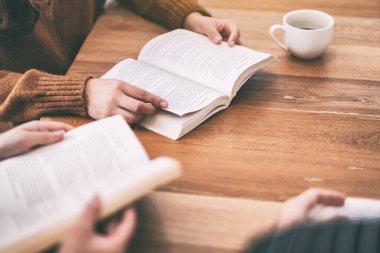 Bir grup insan oturup ahşap masada kitap okumaktan zevk alıyor.