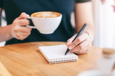 Kahve içerken boş deftere yazan bir kadının yakın plan resmi. 