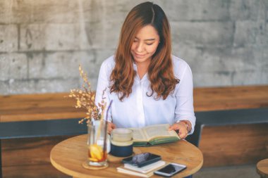 Kafede oturup kitap okuyan Asyalı güzel bir kadının yakın plan görüntüsü.