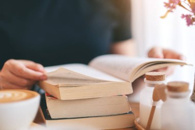 Yakından bakınca, elinde kitap tutan ve kitap okuyan bir kadının resmi. Üzerinde kahve fincanı olan ahşap bir masa.