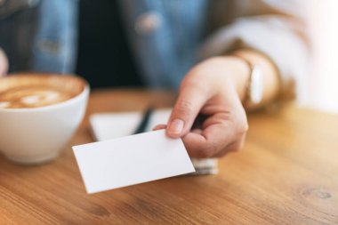Kahve içerken elinde boş bir kartvizit tutan bir kadın.