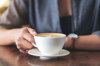 Kafede elinde sıcak kahve tutan ve içen bir kadının yakın plan görüntüsü.