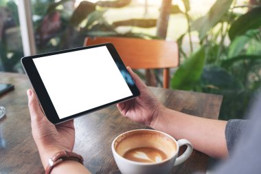 Siyah tabletli, beyaz ekranlı ve ahşap masada kahve fincanı olan bir kadının görüntüsü. 