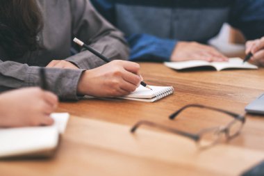 Boş deftere birlikte tahta masaya yazı yazan birçok insanın yakın plan resmi.