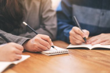 Boş deftere birlikte tahta masaya yazı yazan birçok insanın yakın plan resmi.