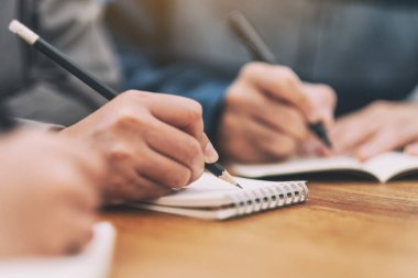 Boş deftere birlikte tahta masaya yazı yazan birçok insanın yakın plan resmi.