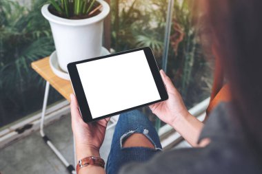 Kafede otururken elinde siyah tablet olan beyaz ekranlı bir kadının görüntüsü.