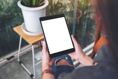 Kafede otururken elinde siyah tablet olan beyaz ekranlı bir kadının görüntüsü.