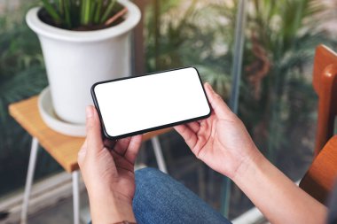 Kafedeki boş masaüstü ekranlı siyah cep telefonu tutan ve kullanan bir kadının görüntüsü