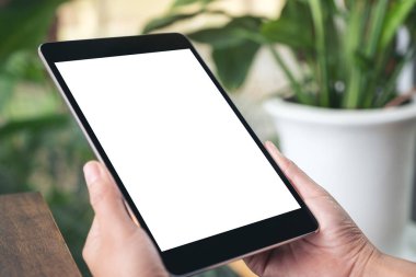 Kafede otururken siyah tableti beyaz ekranla tutan ellerin görüntüsü