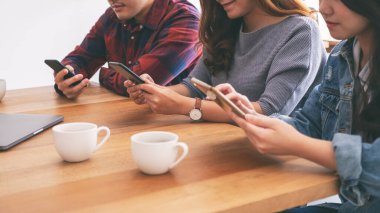 Cep telefonu ve tablet bilgisayar kullanan ve bunlara bakan üç Asyalı genç 