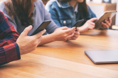 Cep telefonu ve tablet bilgisayar kullanan ve bunlara bakan üç Asyalı genç 