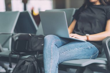 Havaalanında otururken dizüstü bilgisayar kullanan bir kadın gezgin.