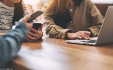 İnsanlar ahşap masadaki cep telefonu ve dizüstü bilgisayara bakıp kullanıyor.