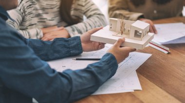 Bir grup mimar, bir mimari modeli ve ofis masasında çizim kağıtlarını tartışıyor.