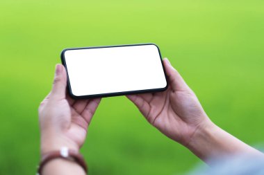 Boş masaüstü ekran ve bulanık yeşil arkaplan ile siyah cep telefonu tutan bir kadının görüntüsü