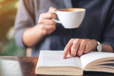Ahşap masada kahve içerken kitap okuyup işaret eden bir kadının yakın plan resmi.