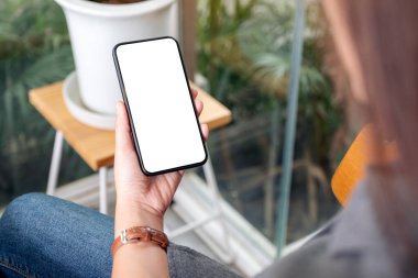 Kafedeki boş masaüstü ekranlı siyah cep telefonu tutan ve kullanan bir kadının görüntüsü